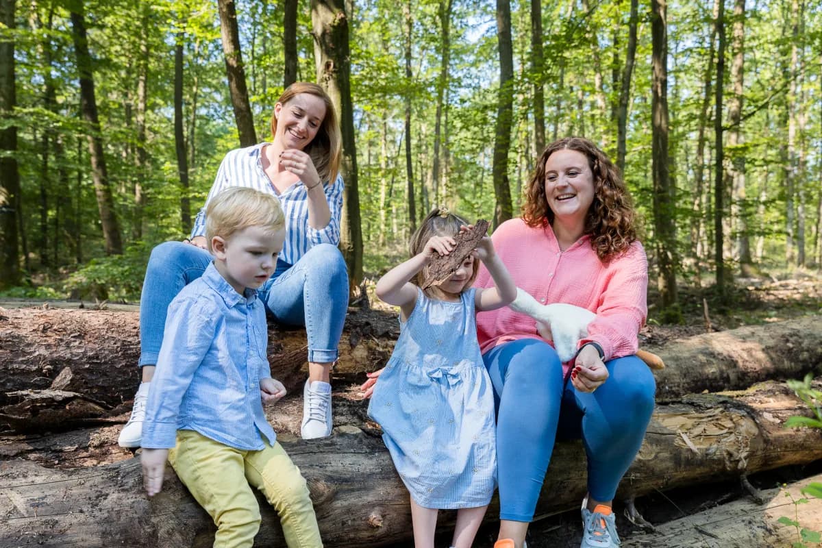 Julia und Eva sitzen mit zwei Kindern auf Baumstämmen im Wald